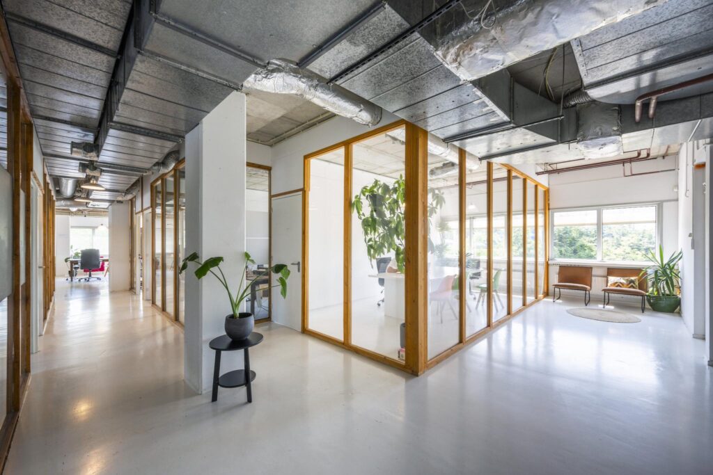 Moderne kantoorruimte aan de Anthony Fokkerweg met glazen vergaderruimtes, planten en industrieel plafond.
